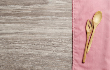 Wooden spoon and fork on pink towel and wood board background