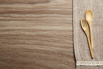 Wooden spoon and fork on brown towel and wood board background
