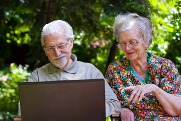Elderly couple having fun with the laptop outdoors