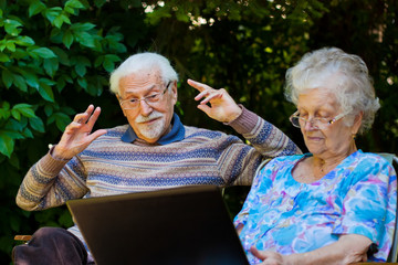 Elderly couple having fun with the laptop outdoors