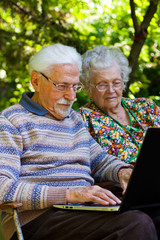 Elderly couple having fun with the laptop outdoors