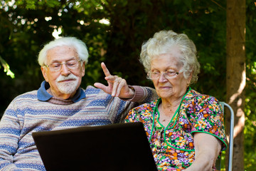 Elderly couple having fun with the laptop outdoors
