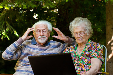 Elderly couple having fun with the laptop outdoors