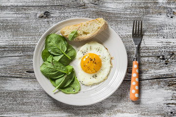 fried egg and fresh spinach on a white plate on a light wooden background