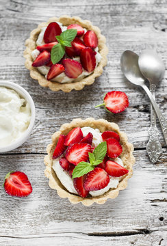 tartlets with cream cheese and strawberries on a light wooden background