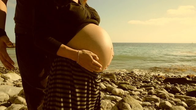 Footage of a pregnant woman on the beach rubbing her bump in sepia/film burn color