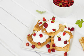 waffles with wild strawberries and whipped cream on white table