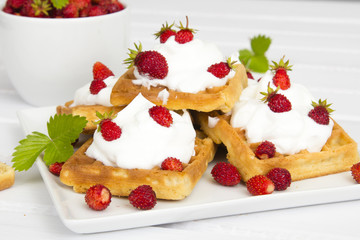 waffles with wild strawberries and whipped cream on white table