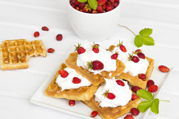 waffles with wild strawberries and whipped cream on white table