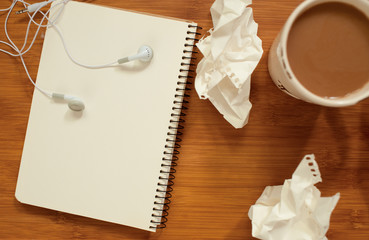 Cup of coffee, crumpled paper, notebook, headphones on wooden table. Top view. Selective focus.