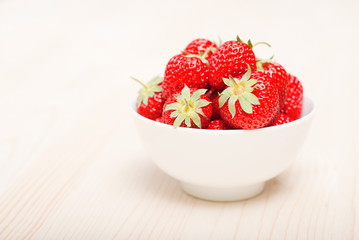 Strawberries in a white bowl on a light table, side view