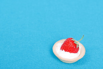 One tartlet with cream and strawberry on a blue background, top
