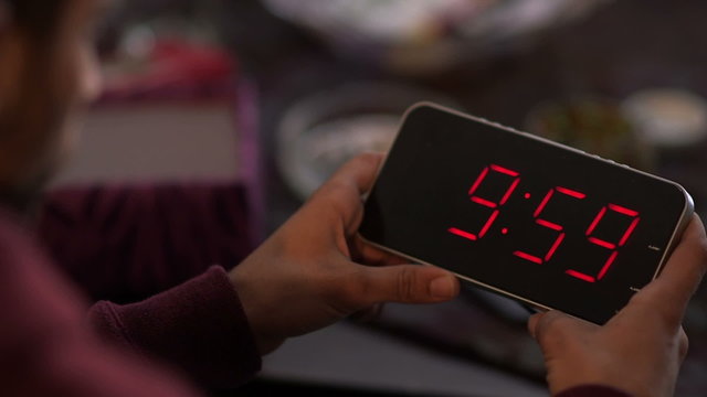 Man holding a digital clock and looking at the time that elapses in it