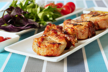 Жареное мясо на белой тарелке и блюдо с зеленью.