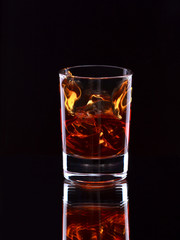 Glass of whiskey with splash on dark background, selective focus