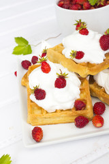 waffles with wild strawberries and whipped cream on white table