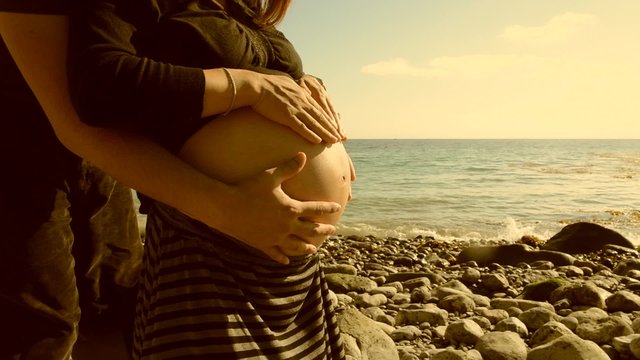 Footage of a pregnant woman on the beach rubbing her bump in sepia/film burn color