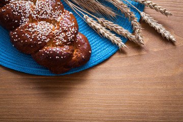 Fresh-baked bun wheat rye ears with blue wattled cover on wooden