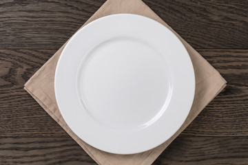 empty white plate on wood table with napkin