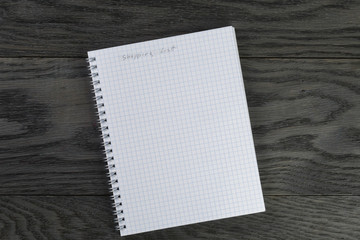 shopping list phrase in notepad with chequered pages on gray