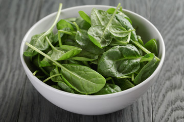 fresh spinach leaves in white bowl on wood table