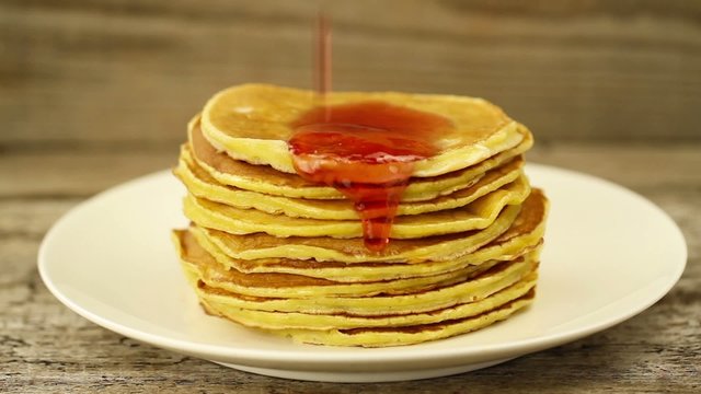honey is poured on a stack of pancakes on wooden background. Breakfast