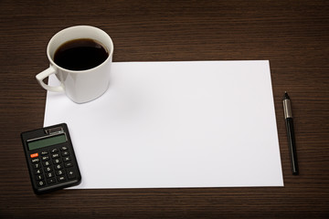 Top view on dark wooden office desk with paper, pen, calculator and cup of coffee.
