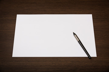 Top view on dark wooden office desk with blank sheet of paper and pen.