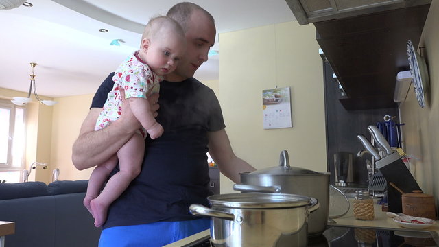 young father together with baby girl  prepare dinner in big pot. Father taste the soup for salt. Fatherhood and baby care at home. Static tripod shot. 4K UHD video clip.