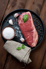 Raw striploin steak with sea salt, pepper and garlic, above view