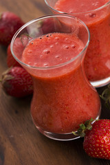 A glass of strawberry smoothie on a wooden background