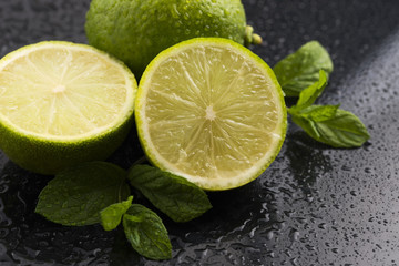 Green limes with mint and water drops on black background