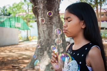 Little asian cute girl playing with bubble wand blowing soap bubbles in the garden background