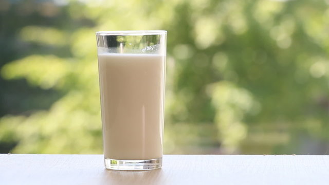  Milk pouring into a glass table on green background.