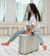 Young woman sitting on her suitcase at home