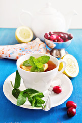 Tea with lemon, mint, and fresh cranberries on a blue background. Selective focus