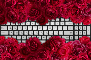 Modern black and chrome laptop keyboard with bush of red rose flowers background