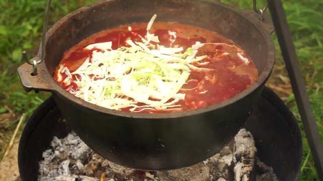 cooking russian national soup borcht on a metal pot on a fireplace