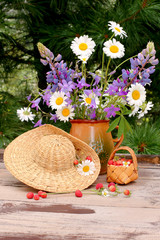 Bouquet of summer flowers with straw hat and wild strawberries 