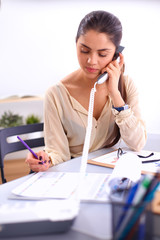 Young businesswoman sitting at the desk and talking on phone