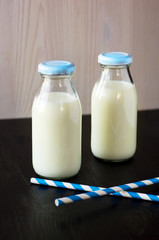 Two retro bottles of milk with striped straws standing on old ta