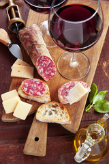 two wineglass with red wine and assortment of cheese and salami.