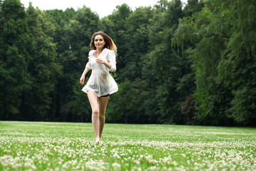 Young beautiful girl in the white shirt is running on the green