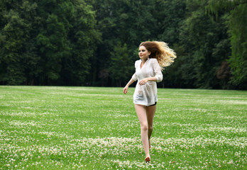 Young beautiful girl in the white shirt is running on the green