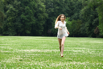 Young beautiful girl in the white shirt is running on the green