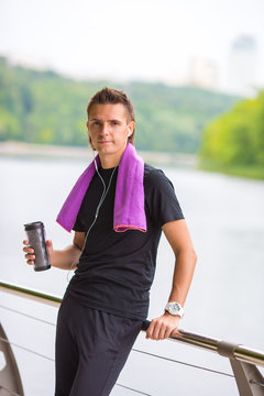 Young sports man with towel and bottle of water after jogging