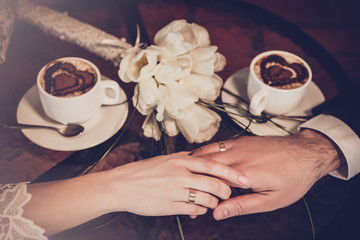 Two cups of coffee and hand of bride and groom with wedding rings