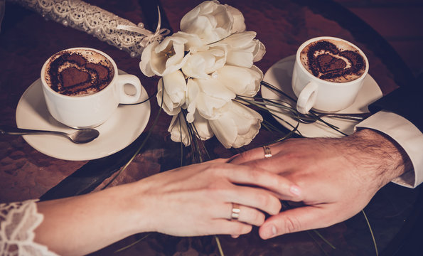 Two cups of coffee and hand of bride and groom with wedding rings