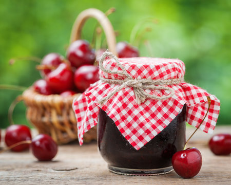 Jars of jam and basket with cherry on background.