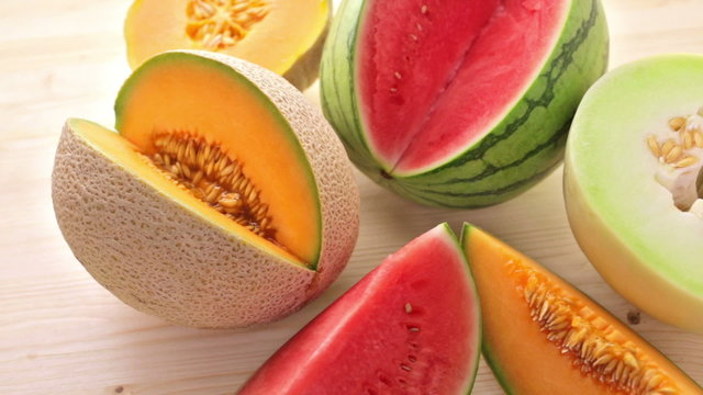 Variety of organic melons sliced on wood table.